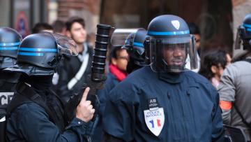 Two police officers in the foreground, one armed with a large tear gas launcher
