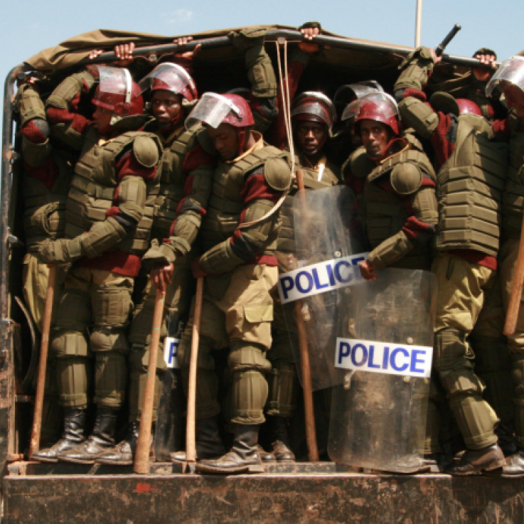 Un grand nombre de policiers armés de clubs attendent de sauter d'une camionnette au Kenya. La police porte beaucoup d'armures, de boucliers, de casques et de matraques.