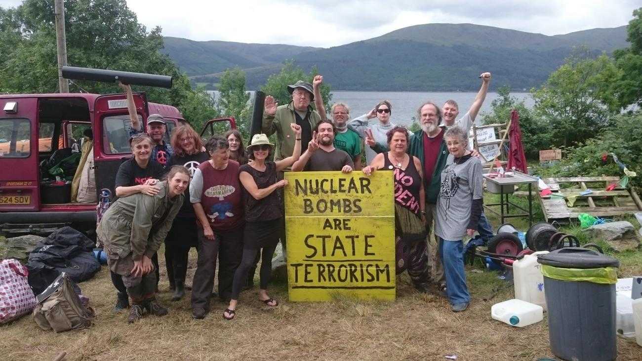 Gathering of people at the Coulport Disarmamnet camp. People hold a banner saying 'Nuclear weapons are state terrorism'