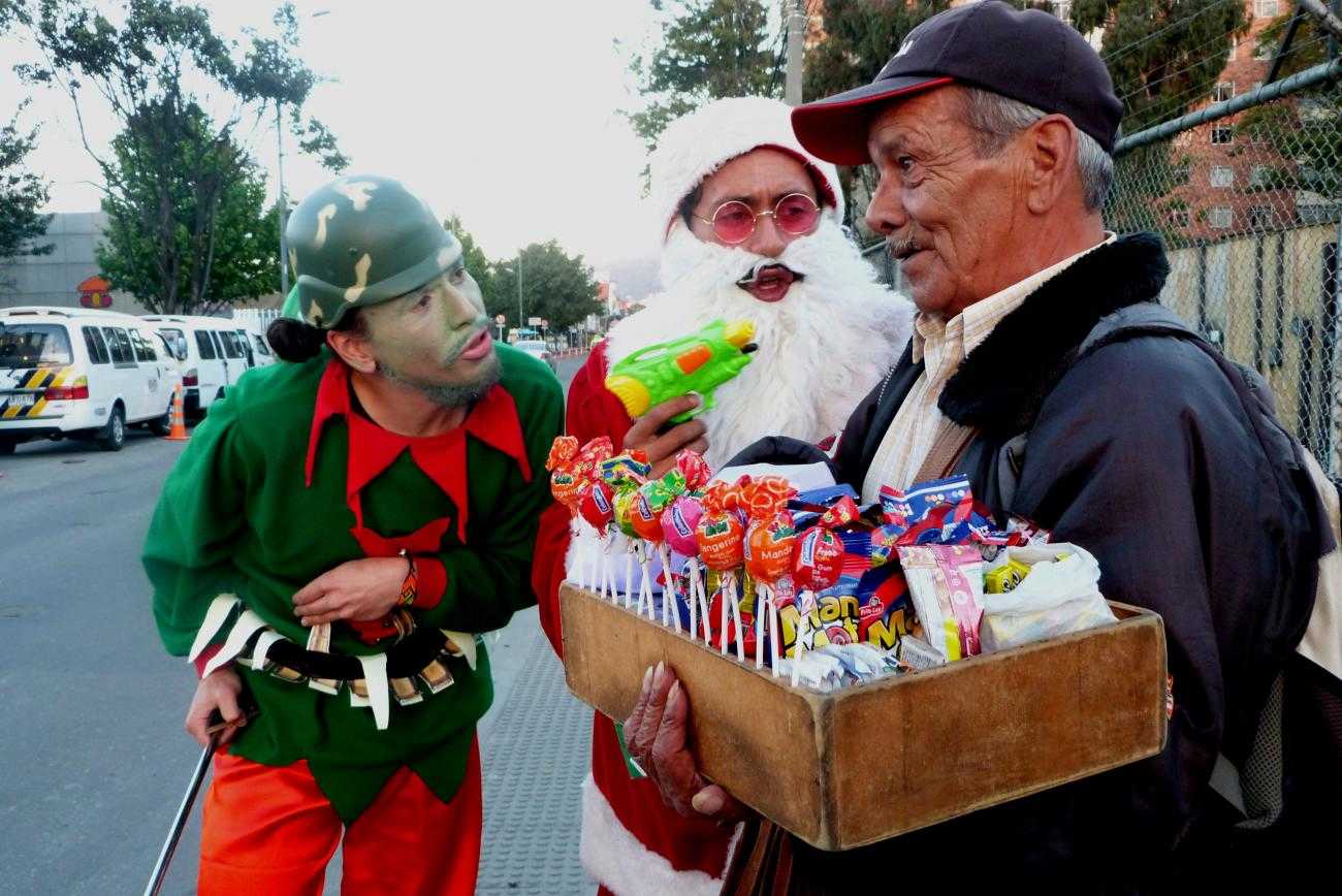 Activistas antimilitaristas entrevistan a miembros del público disfrazados de santa y elfos navideños, armados con pistolas de agua y cascos militares