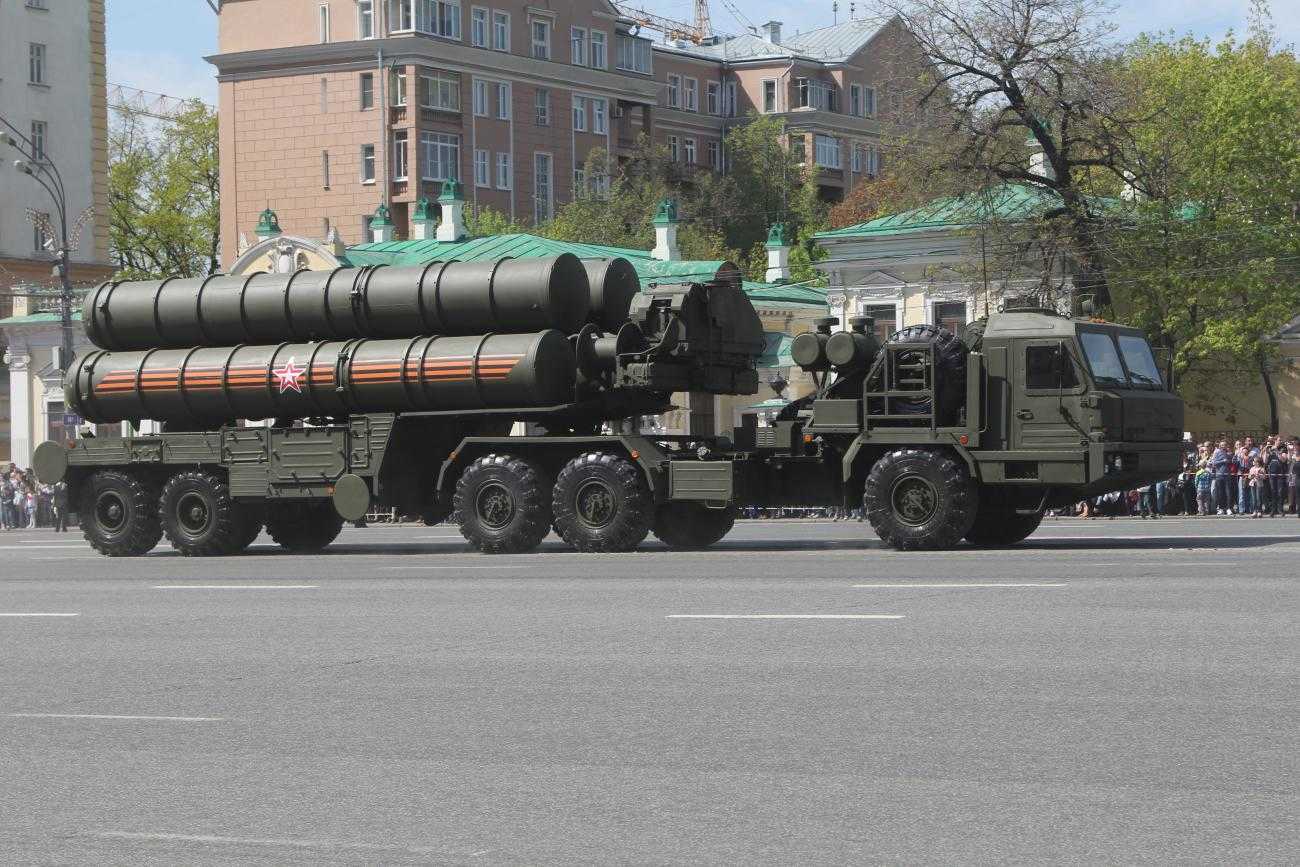 A large truck pulls an even larger trailer. On the trailer are several large missile launchers. Everything is painted dark khaki green