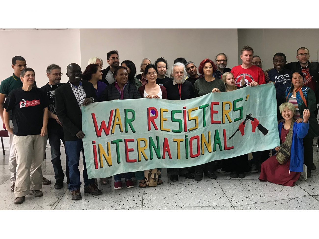 Dos docenas de personas se paran detrás de una pancarta que dice "Internacional de Resistentes a la Guerra"
