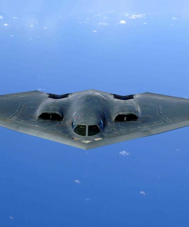 A Northrop Grumman B2 bomber, flying over an ocean. The plane is black, and very aerodynamically shaped.