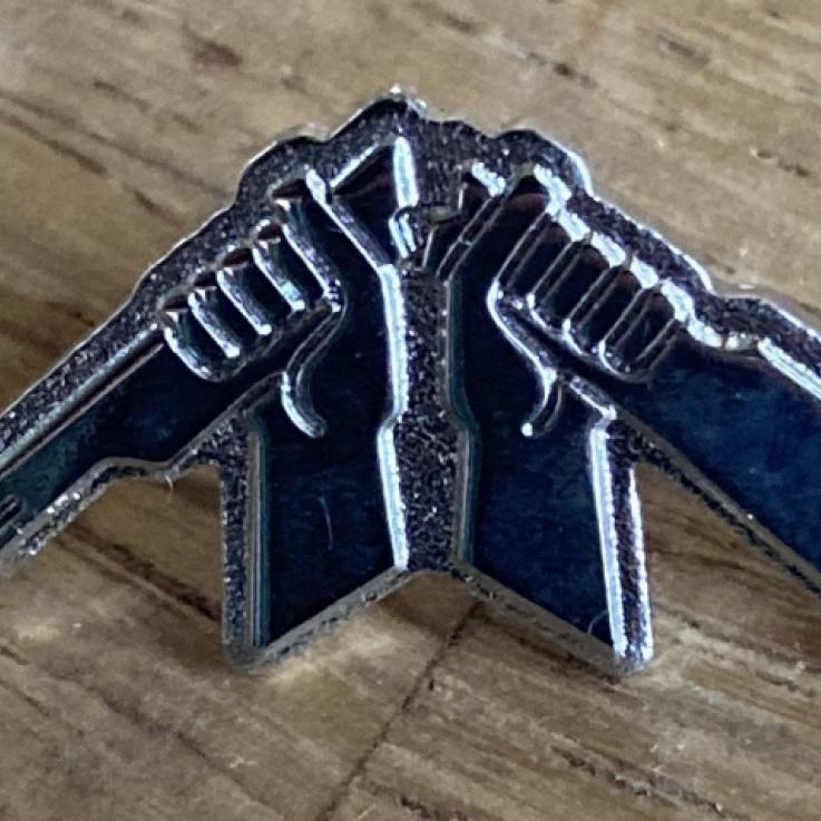 A silver broken rifle pin badge